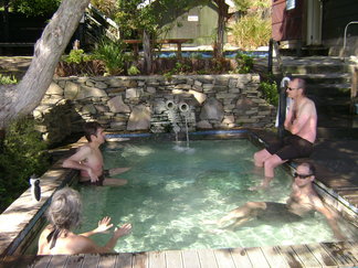 Side view of people sitting across from each other, in an outdoor hot tub that's shaded by trees